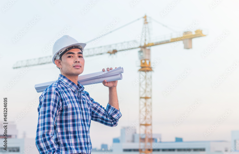 Portrait of engineer wear white safety helmet and holding the blueprint at construction site with crane background Portrait of engineer wear white safety helmet and holding the blueprint at construction site with crane background
