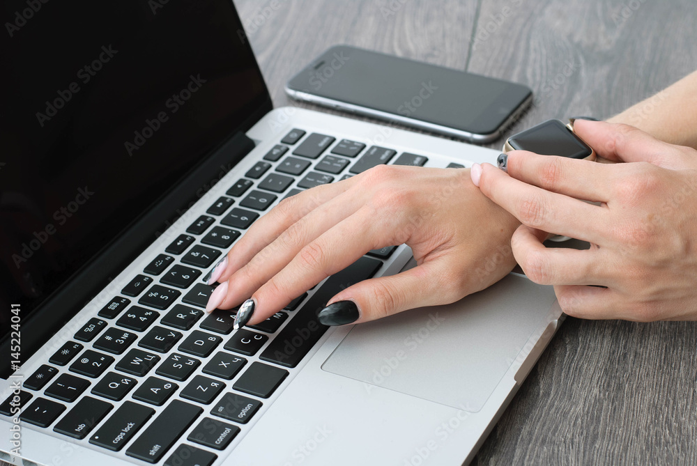 Female hand with smartwatch with holding mobile phone on laptop computer Female hand with smartwatch with holding mobile phone on laptop computer