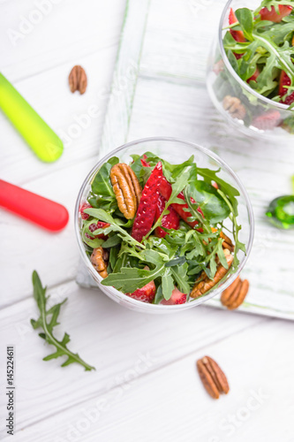 Fresh salad with strawberries, arugula and pecans on a white wooden background. Concept of Healthy Food. Top view