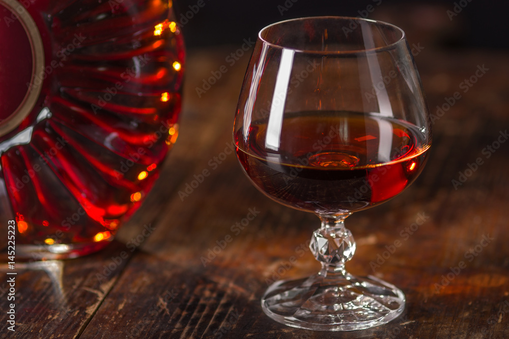 Glass of cognac and  bottle of cognac on vintage wooden background. Low depth of field.