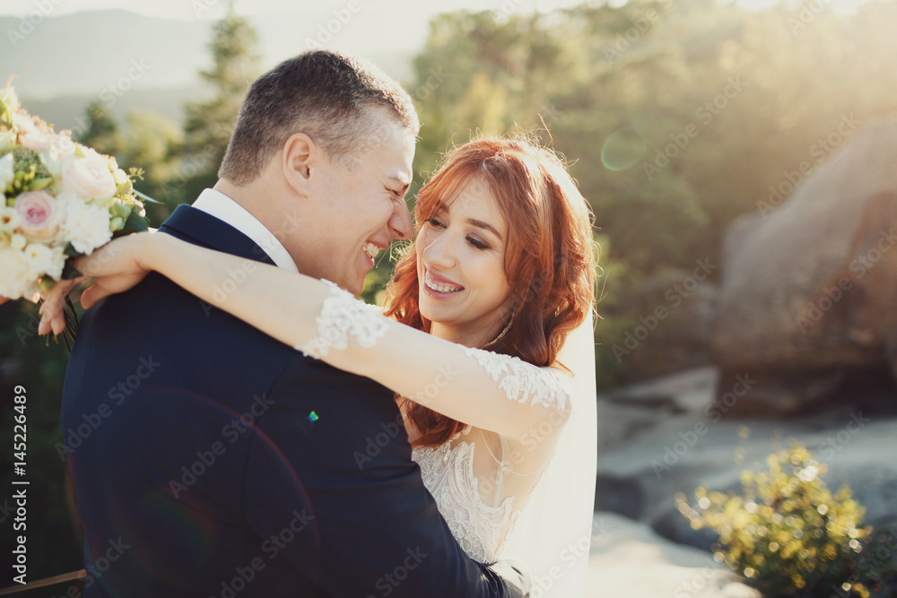 Laughing wedding couple stands in golden rays of evening sun Laughing wedding couple stands in golden rays of evening sun