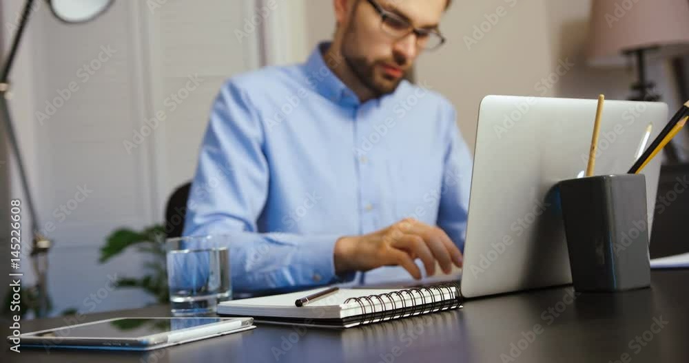 Young business man writing in his notebook on office background. Attractive man working in office. Young business man writing in his notebook on office background. Attractive man working in office.