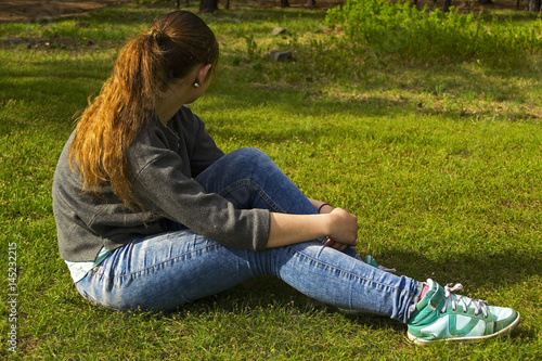 The thoughtful girl sits on a grass.