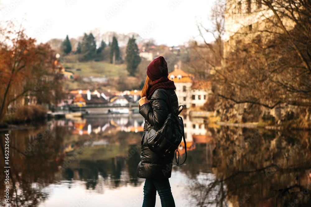 
The girl tourist with backpack standing on the shore and enjoy the nature and views of the city. The reflection in the water. The concept of travelling solo


