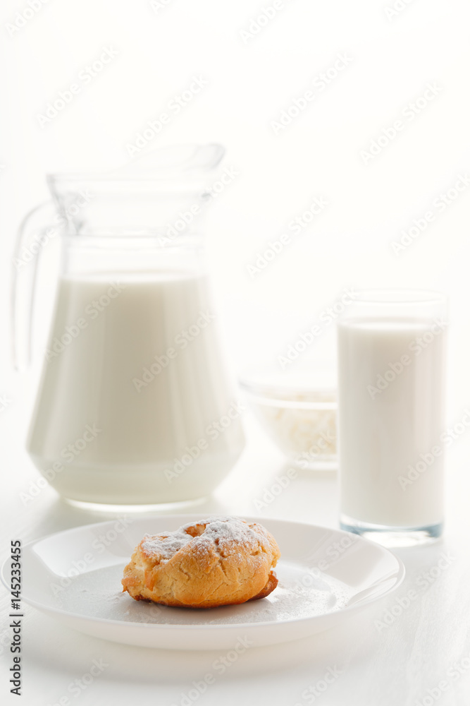 Eclair cake in a plate, with milk in a glass and jug, cottage cheese in a bowl in the background, on a white table, in a high key, with space for text Eclair cake in a plate, with milk in a glass and jug, cottage cheese in a bowl in the background, on a white table, in a high key, with space for text