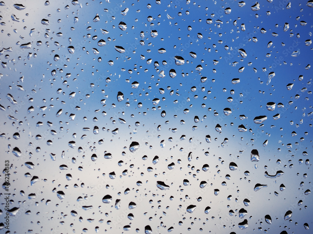 Water drops at the window glass at the blue sky with the clouds background Water drops at the window glass at the blue sky with the clouds background