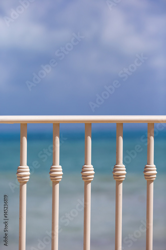 View to the sea from the balcony. Metal poles. Turquoise water in the background. 
