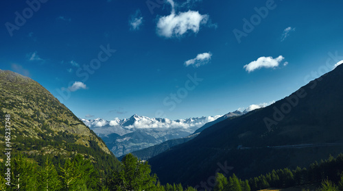 Snow capped mountains under deep blue sky. View from the valley through the forest and trees