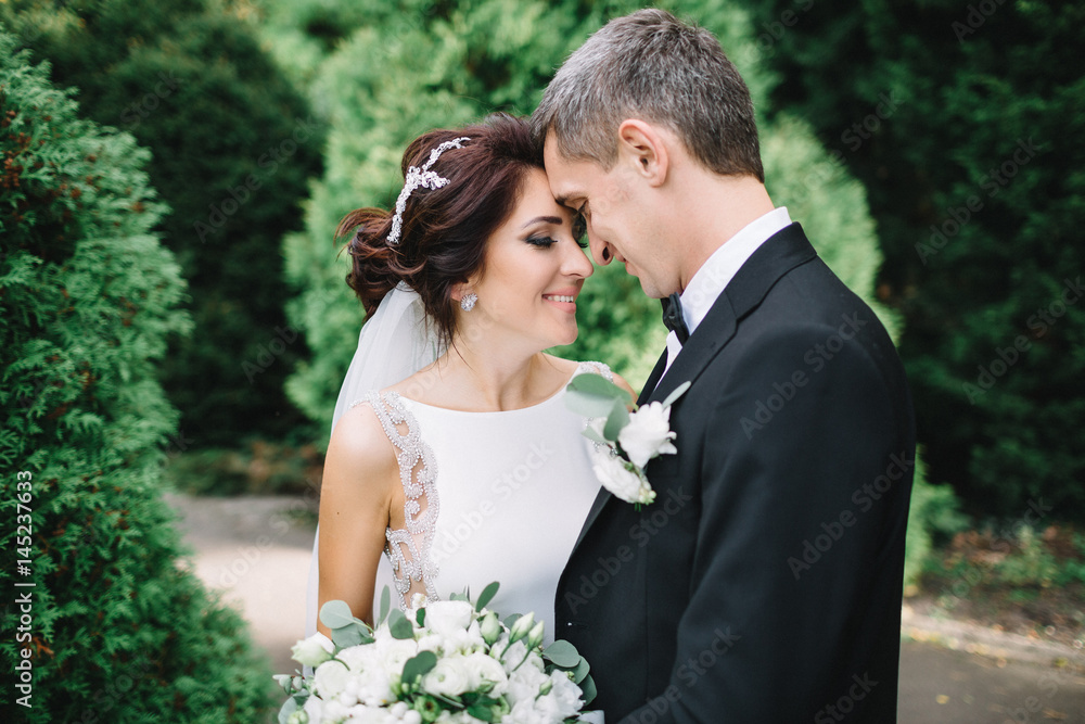 Green trees surround wedding couple leaning to each other tender Green trees surround wedding couple leaning to each other tender