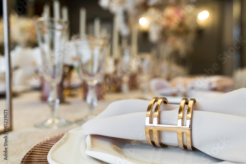 Golden ring holds white napking which lies on dinner table photo