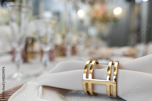 Golden ring holds white napking which lies on dinner table