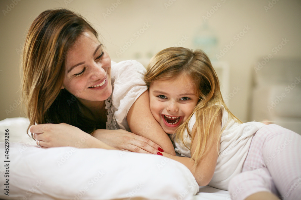 Mother with her cute little daughter lying on bed.