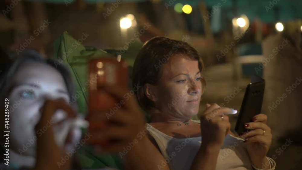 Two female friends browsing internet on smartphones sitting in cafe at night
Two female friends browsing internet on smartphones sitting in cafe at night