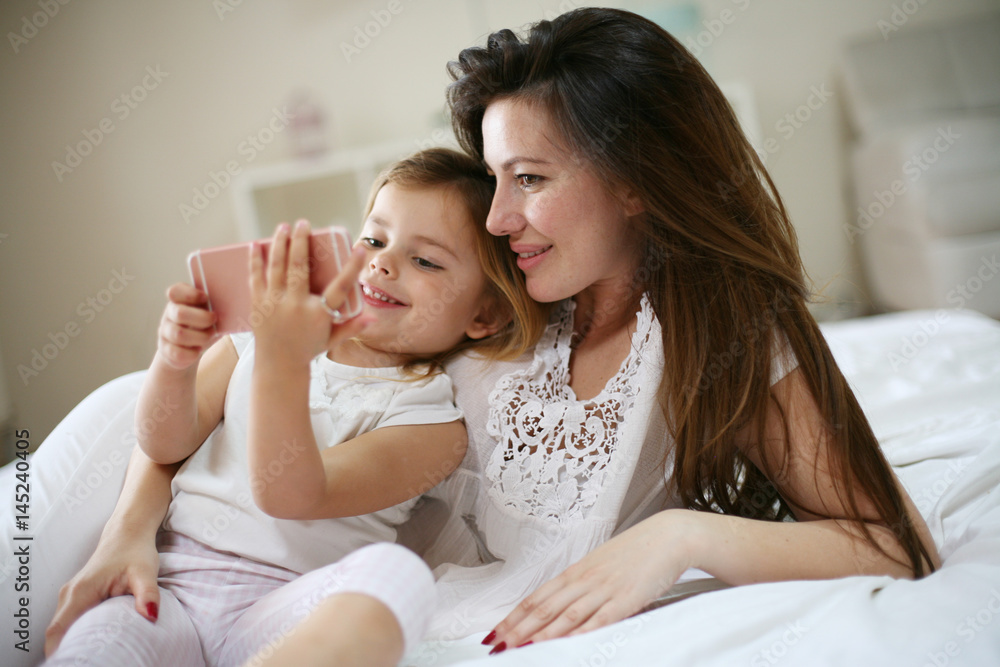 Smiling mother with daughter using smart phone on bed. Smiling mother with daughter using smart phone on bed.