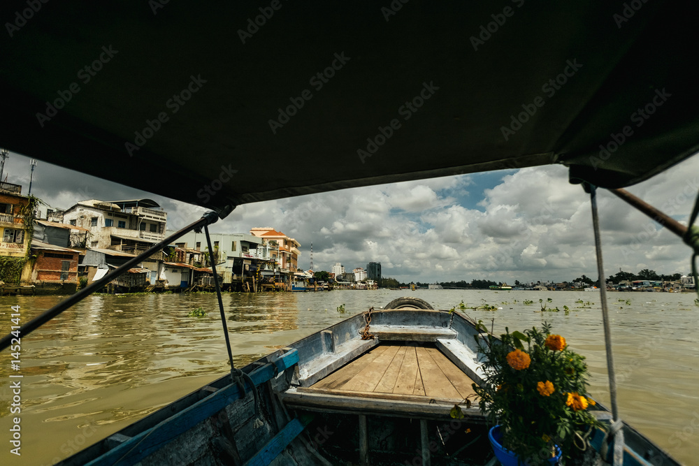 Blue boat with yellow flowers goes between grey house in Vietnam