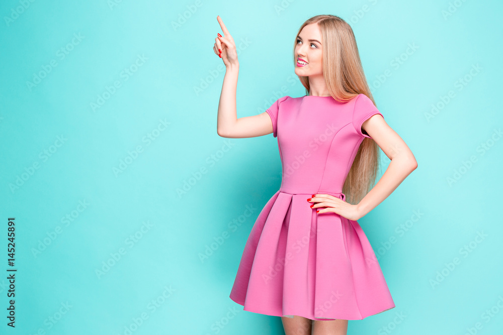 Smiling beautiful young woman in pink mini dress posing, presenting something Smiling beautiful young woman in pink mini dress posing, presenting something