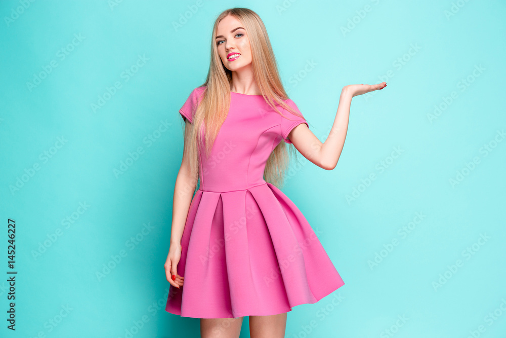 Fototapeta premium Smiling beautiful young woman in pink mini dress posing, presenting something