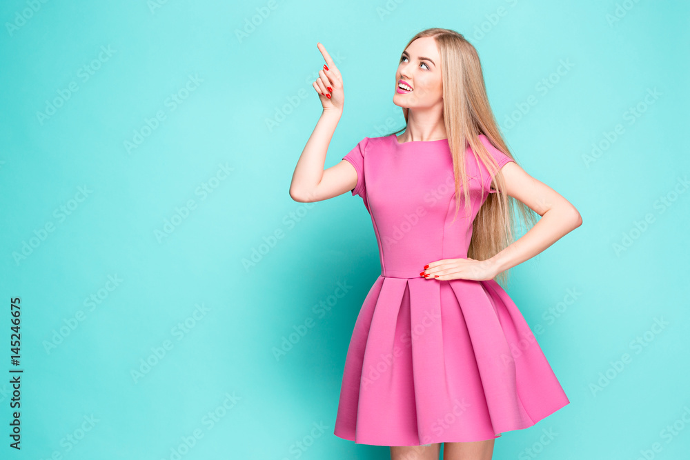 Fototapeta premium Smiling beautiful young woman in pink mini dress posing, presenting something