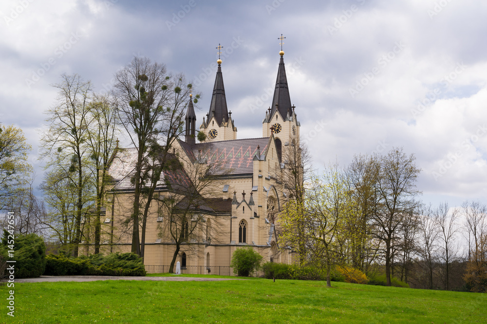 Church of the Nativity of the Virgin Mary, Orlova, Silesia, Czech Republic / Czechia - neo-gothic sacral building in beautiful green park during spring. Cloudy sky