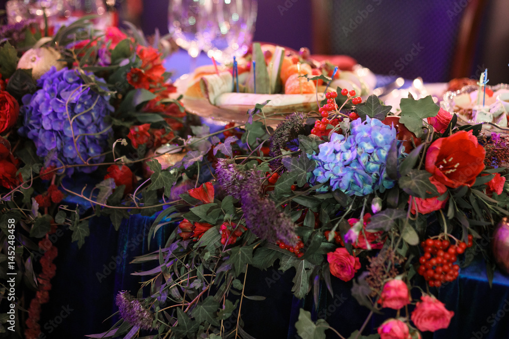 Garland of roses, blue hydrangeas and greenery lies on dinner table