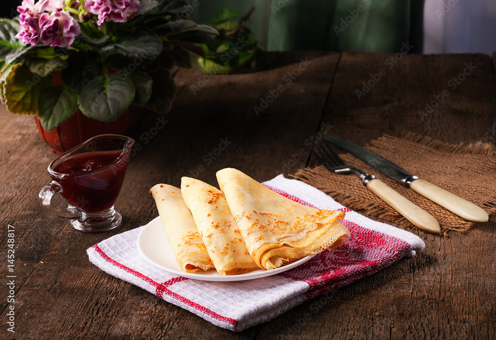 Homemade wheat crepes or pancakes with strawberry jam or marmalade stacked on a plate on a wooden rustic table