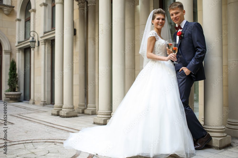 Fototapeta premium Bride and groom stand by each other with glasses of champagne