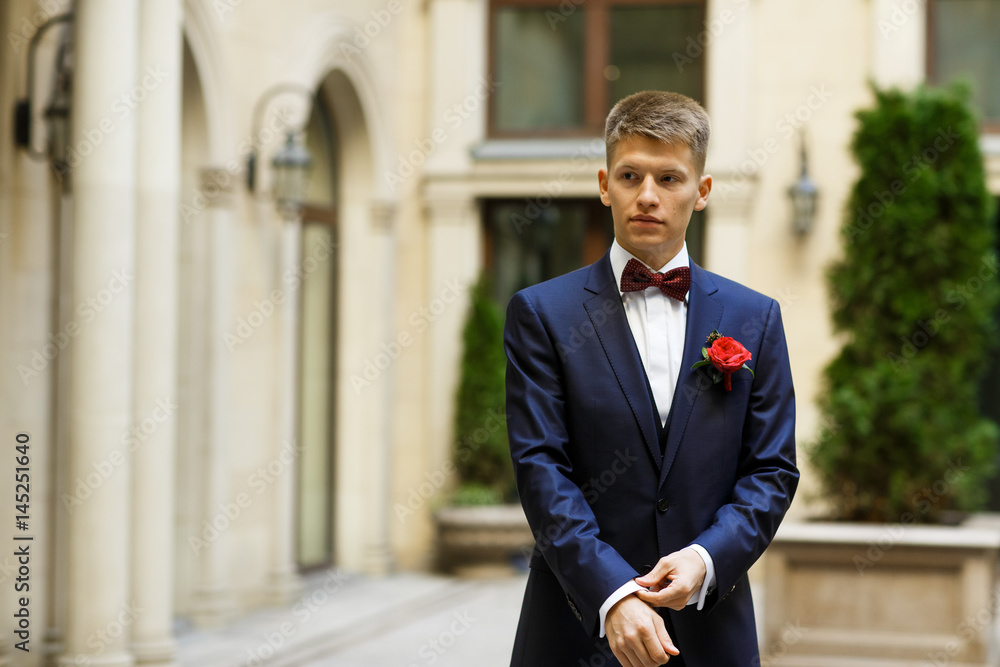 Young groom in blue suit walks around the backyard Young groom in blue suit walks around the backyard
