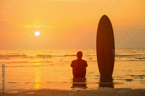 Vacation Concept ; Happy Asian surfer sitting with surfboards on the beach at sunset,Phuket,Thailand