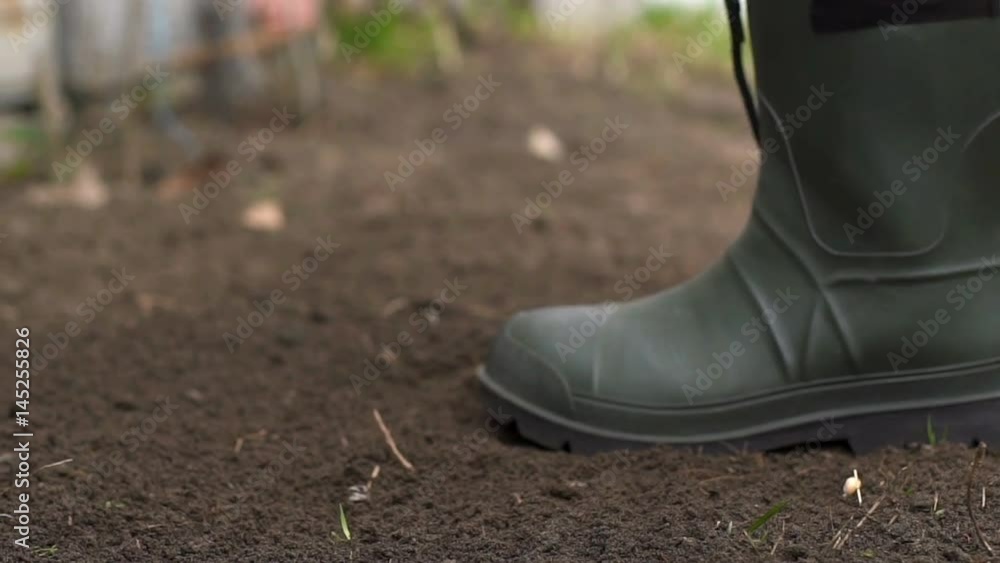 Gardener wearing rubber boots raking soil on sunny day. Slow motion Gardener wearing rubber boots raking soil on sunny day. Slow motion