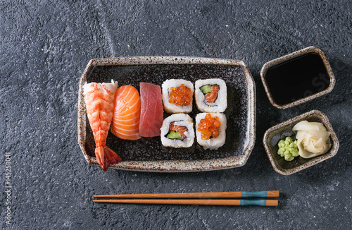 Sushi Set nigiri and sushi rolls in dark ceramic plate with soy sauce and chopsticks over black stone texture background. Top view with space. Japan menu