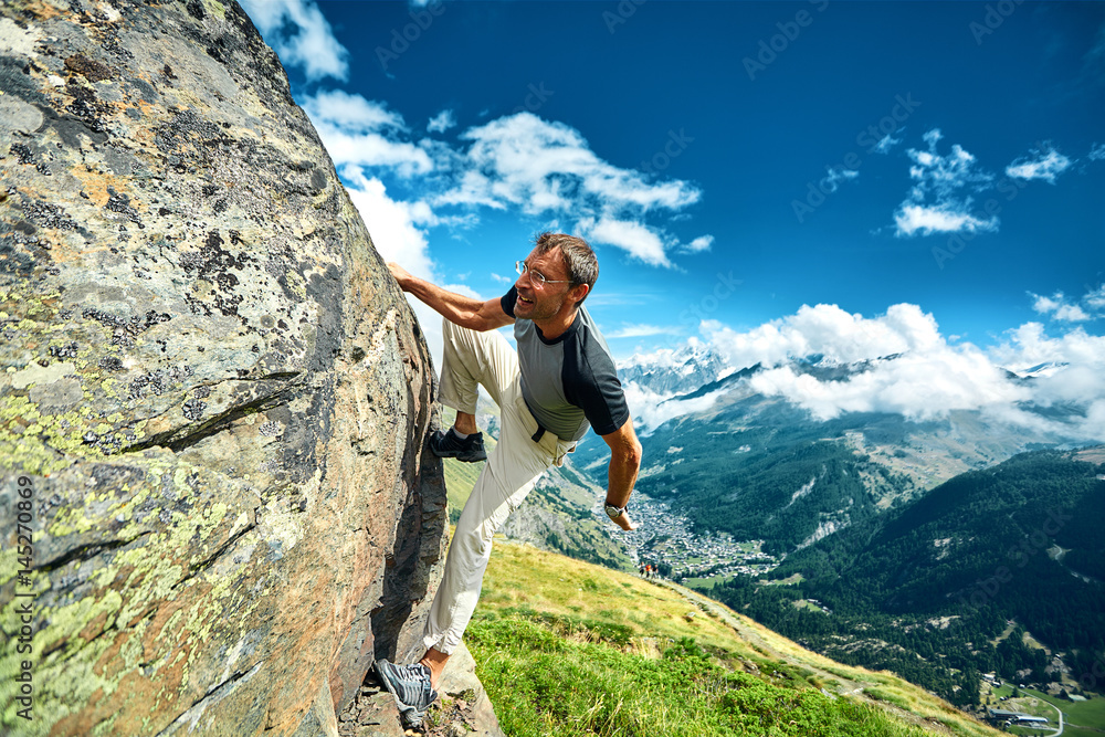 Adult man climbs on a rocky wall, against a blue sky