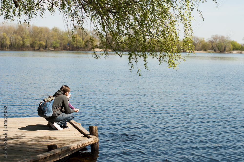 Father and son on a wooden pier near the river Father and son on a wooden pier near the river