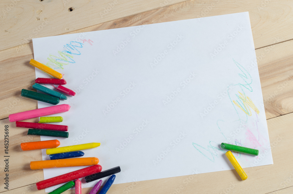 Wax crayons on white sheet, wooden background Wax crayons on white sheet, wooden background