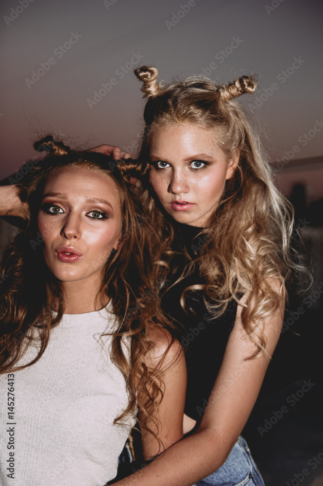 Obraz premium lifestyle and people concept: Fashion portrait of two stylish girls best friends wearing jeans skirts, outdoors on the roof. Happy summer time for fun.