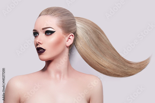 Beautiful young blonde girl with high ponytail. Bright makeup, black arrows, purple lips. Beauty, fashion, health, beauty salon, spa, hairstyle. Smooth skin. Cosmetics.