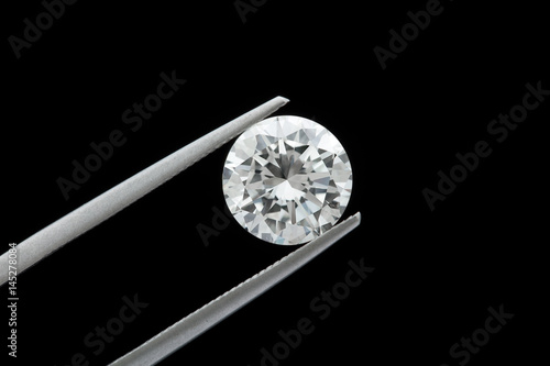 Фототапет loose brilliant round diamonds is being held by tweezers on black background