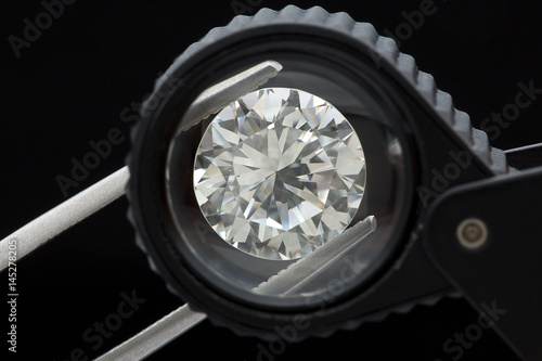loose brilliant round diamonds is being held by tweezers and looked through a black loupe