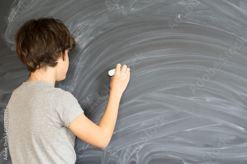 Teen Boy with chalk in hand writting on empty black board