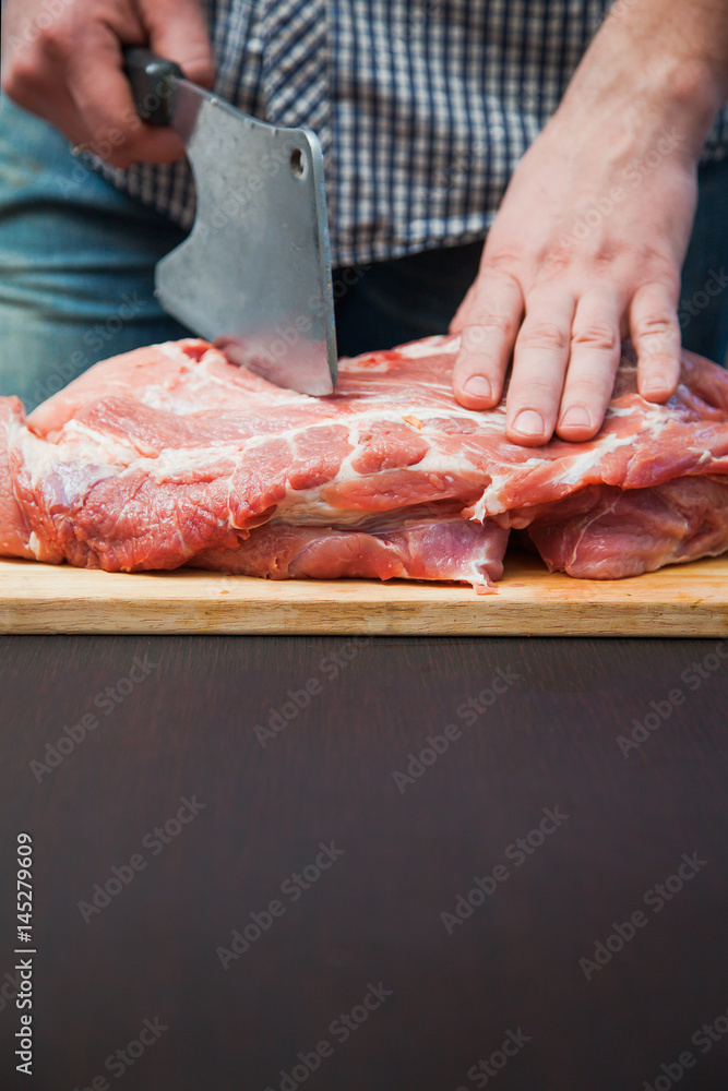 Piece of pork neck cutout on woodwn table. Man cutting meat