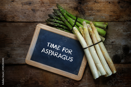 Green and white asparagus and a  blackboard with text time for asparagus, on a rustic wooden background, top view from above, copy space