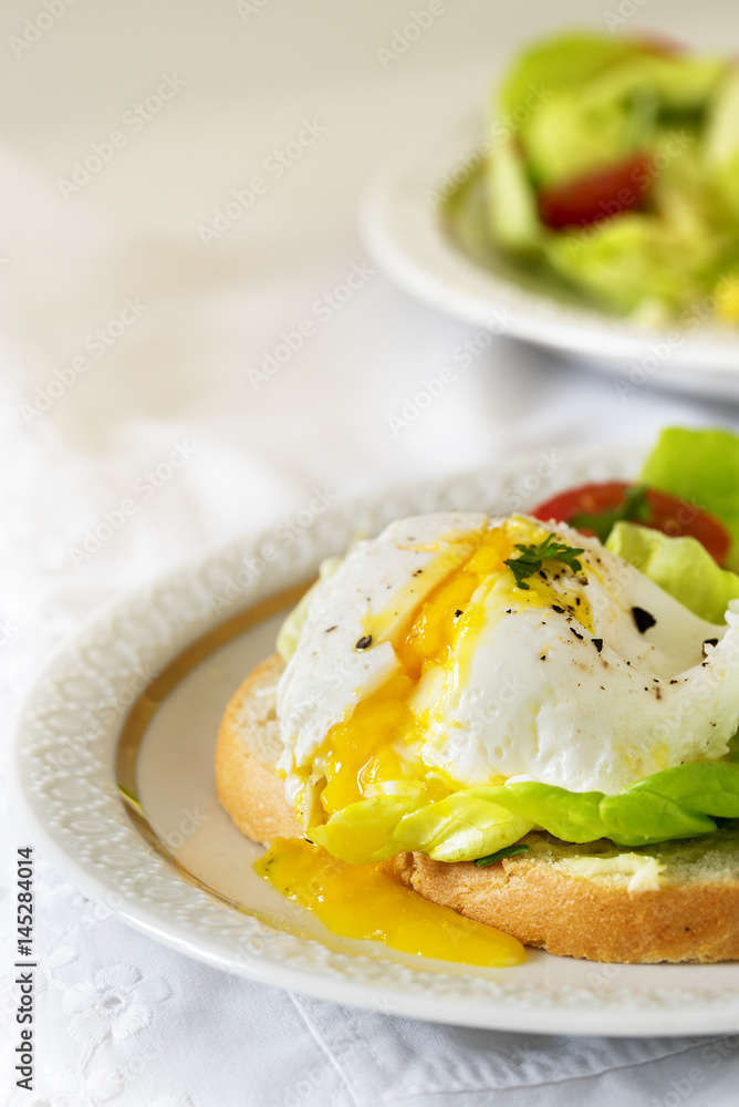 Poached egg with running yolk on baguette slice with salad and tomatoes on a white plate, vertical, copy space Poached egg with running yolk on baguette slice with salad and tomatoes on a white plate, vertical, copy space