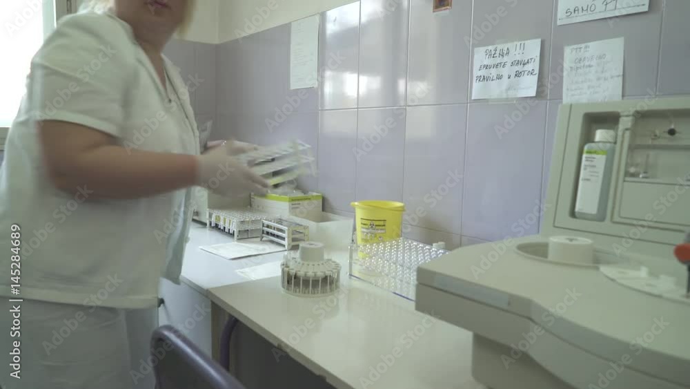 Laboratory technician in white suit putting test tubes with blood samples in a container for analysis of coagulation, dolly shot to the woman, indoors Laboratory technician in white suit putting test tubes with blood samples in a container for analysis of coagulation, dolly shot to the woman, indoors