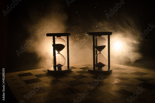 Time concept. Silhouette of Hourglass clock and smoke on dark background with hot yellow orange lighting, or symbols of time with copy space, sandglass or sand clock