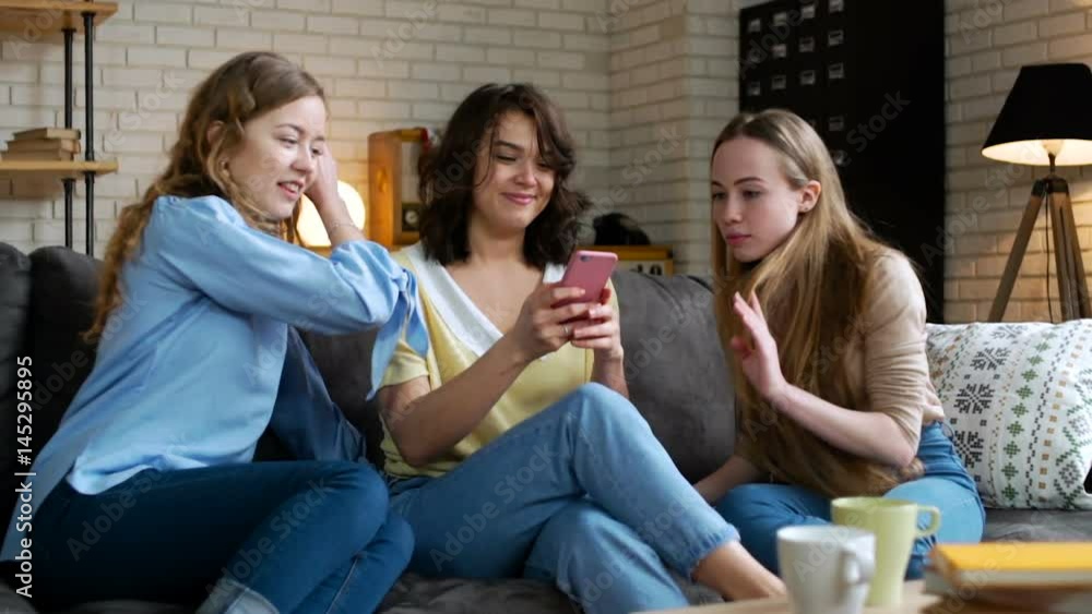 three young and energetic best friend girls look over photos in social network using telephone mobile and discuss emotionally, laughing and impressing surprise sitting on sofa at home during sunny day three young and energetic best friend girls look over photos in social network using telephone mobile and discuss emotionally, laughing and impressing surprise sitting on sofa at home during sunny day