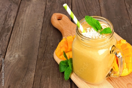 Mango coconut smoothie in a mason jar glass on paddle board against a rustic wood background photo