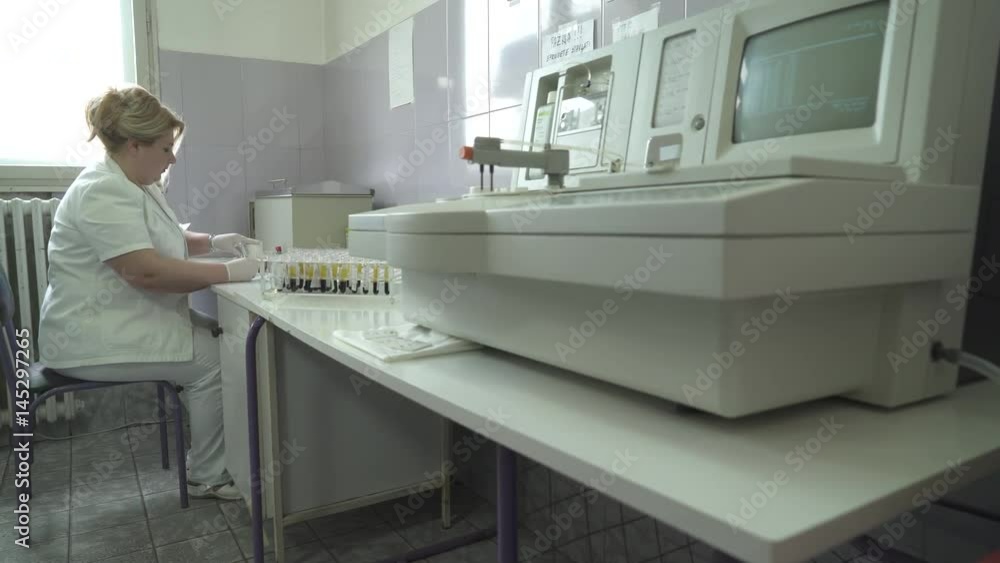 Caucasian laboratory technician in white suit sits and takes test tubes with blood samples, worker writes results after analysis, dolly tracking shot, close up, indoors Caucasian laboratory technician in white suit sits and takes test tubes with blood samples, worker writes results after analysis, dolly tracking shot, close up, indoors