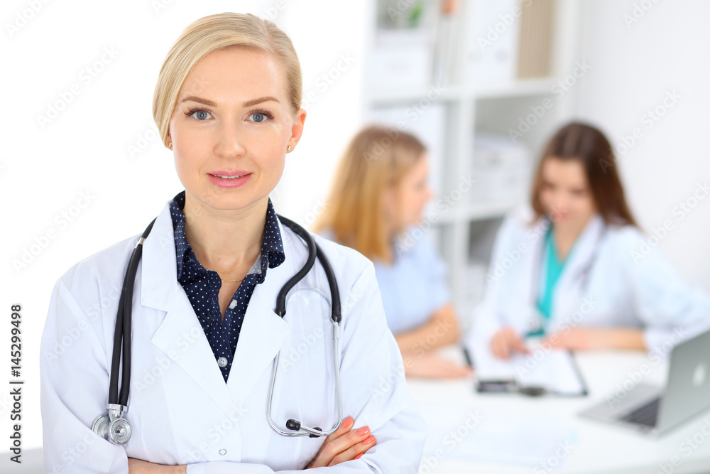 Female doctor smiling on the background with patient and his physician in hospital Female doctor smiling on the background with patient and his physician in hospital