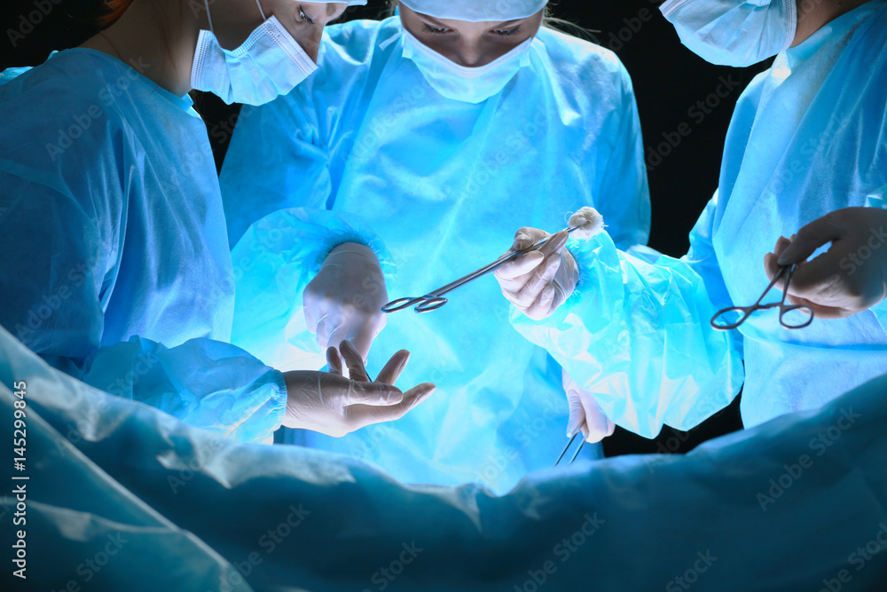 Group of surgeons at work in operating theater toned in blue. Medical team performing operation Group of surgeons at work in operating theater toned in blue. Medical team performing operation
