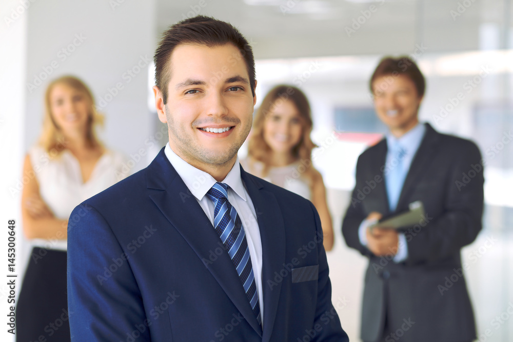Smiling businessman in office with colleagues in the background. Smiling businessman in office with colleagues in the background.