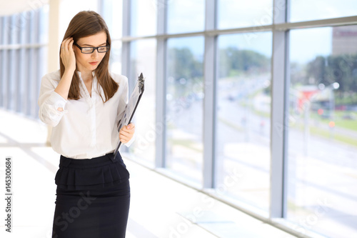 Modern business woman standing and keeping a clipboard in the office.